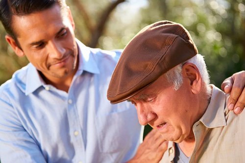 Мужчина держит пожилого мужчину за плечи